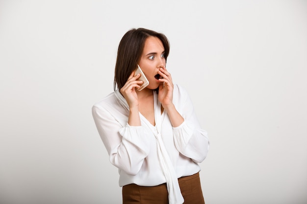 Schockierte elegante Frau, die Telefon spricht und klatscht