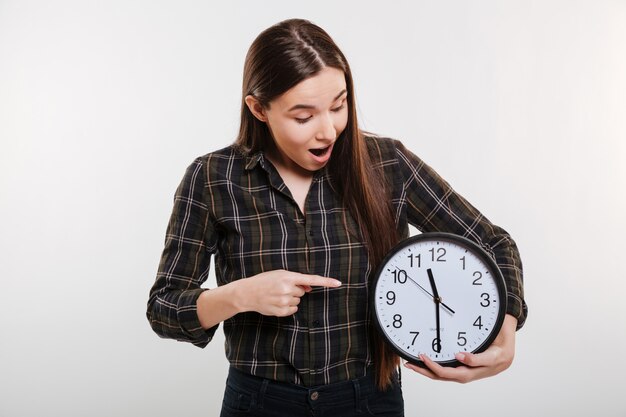 Schockierte Frau im Hemd, das die Uhr hält