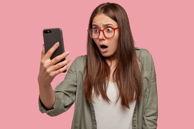 Schockierte Frau sieht peinliches Bild auf dem Bildschirm des Smartphones