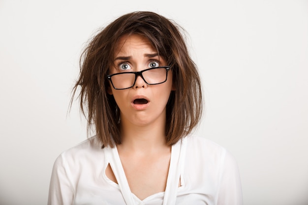 Schockierte keuchende Frau in Brille mit unordentlichem Haar