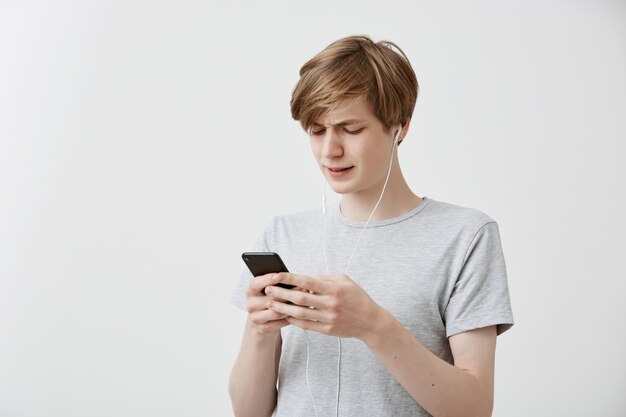 Schockierte verwirrte Hipster-Typ-Nachrichten mit Freunden, nutzt die kostenlose Internetverbindung auf einem modernen Handy und erhält schlechte Nachrichten. Erstaunter junger Mann erhält schlechte Nachrichten. Menschliche Gefühle, Emotionen, Reaktionen
