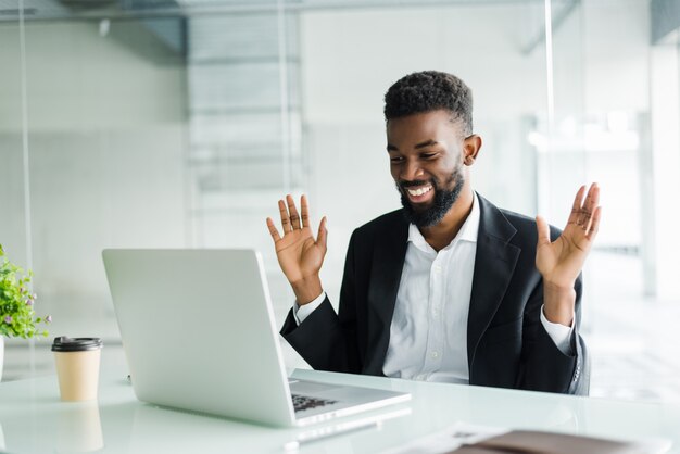 Schockierter afroamerikanischer Geschäftsmann im Anzug, der sich von Online-Nachrichten betäubt fühlt, die auf Computerbildschirm schauen, der mit Laptop am Arbeitsplatz sitzt, gestresster Händlerinvestor überrascht von Börsenveränderungen