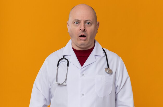 Schockierter erwachsener slawischer Mann in Arztuniform mit Stethoskop nach vorne