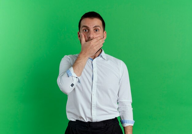 Schockierter gutaussehender Mann legt Hand auf Mund lokalisiert auf grüner Wand