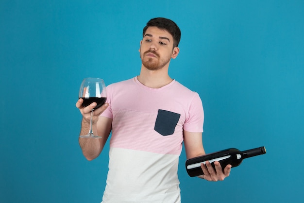 Schockierter junger Mann, der ein Glas Wein betrachtet.
