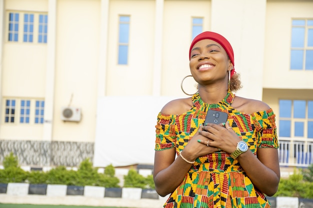 Schöne afrikanische Dame, die ihr Handy voller Freude an ihre Brust hält
