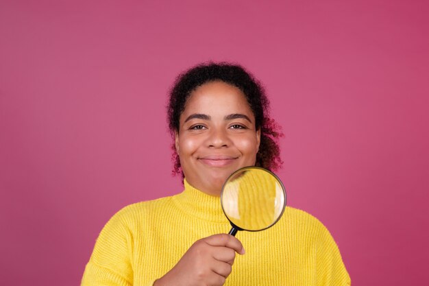 Schöne afroamerikanische Frau auf rosa Wand mit Lupenlächeln und Blick auf die Kamera