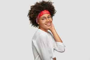Kostenloses Foto schöne afroamerikanische frau steht im profil, lässig gekleidet, hat ein breites strahlendes lächeln, ist glücklich, fotografiert zu werden, isoliert über weißer wand. positives emotions- und gefühlskonzept