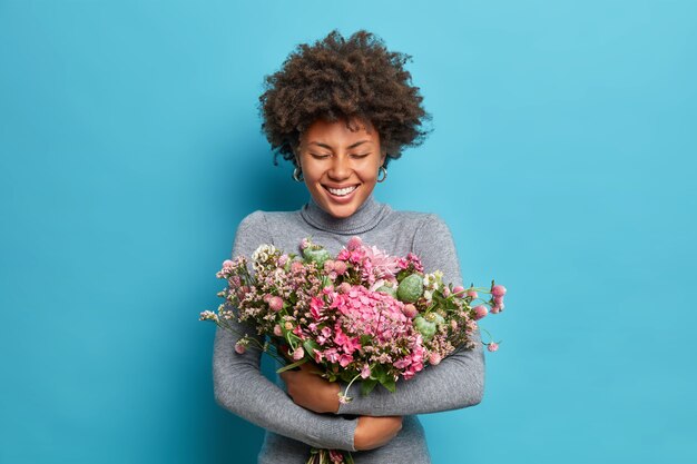 Schöne afroamerikanische Frau umarmt Blumenstrauß bekommt Frühlingsblumen