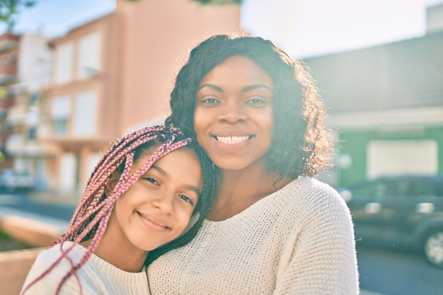 Schöne afroamerikanische Mutter und Tochter lächeln glücklich und umarmen sich. Stehend mit einem Lächeln im Gesicht, das in der Stadt steht.