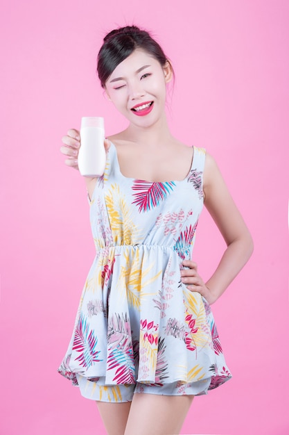 Schöne asiatische Frau, die eine Flasche des Produktes auf einem rosafarbenen Hintergrund anhält.
