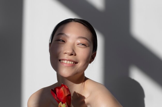 Schöne asiatische Frau, die eine Rose mit perfekter Haut hält