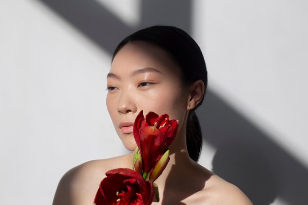 Schöne asiatische Frau, die eine Rose mit perfekter Haut hält