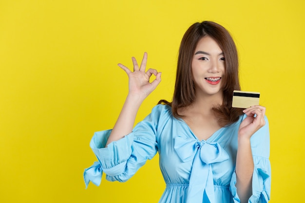 Schöne asiatische Frau, die Kreditkarte auf gelber Wand zeigt
