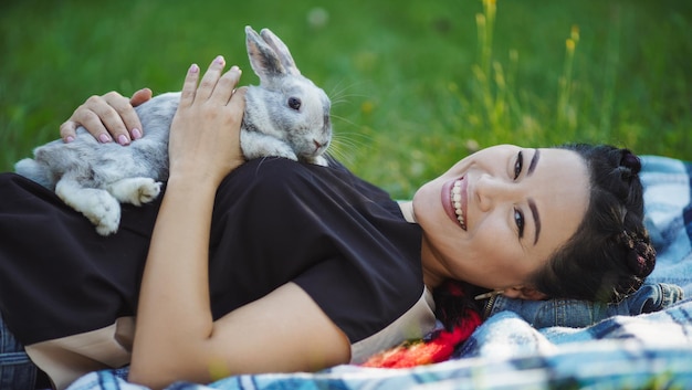 Kostenloses Foto schöne asiatische frau, die mit flauschigem kaninchen auf grünem gras liegt