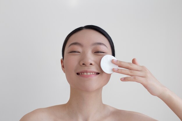 Schöne asiatische Frau, die mit Gesichtscreme aufwirft