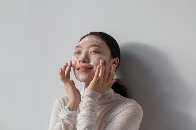 Schöne asiatische Frau, die mit Gesichtscreme aufwirft