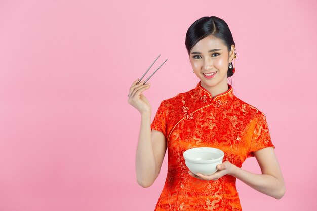 Schöne asiatische Frau glückliches Lächeln und Essen im chinesischen Neujahr auf rosa Hintergrund.