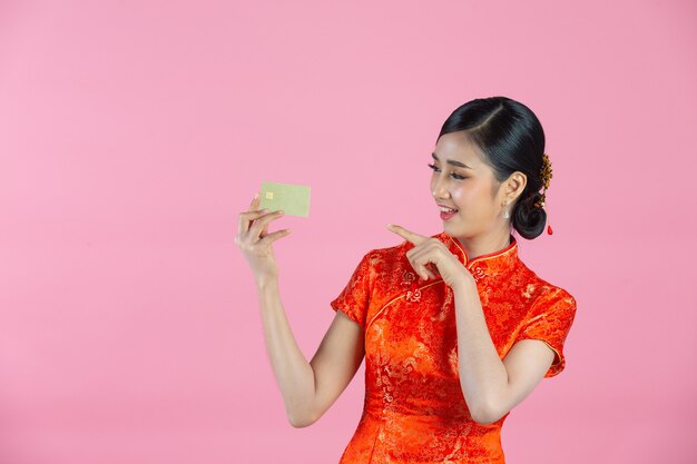 Schöne asiatische Frau glückliches Lächeln und Kreditkarte im chinesischen Neujahr auf rosa Hintergrund zeigen.