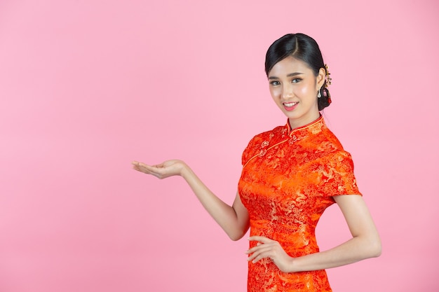 Schöne asiatische Frau glückliches Lächeln und zeigt Ihnen etwas im chinesischen Neujahr auf rosa Hintergrund
