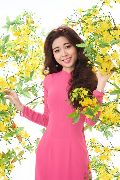 Schöne asiatische Frau im rosafarbenen Kleid, das im blühenden Busch steht