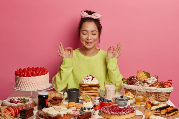 Schöne asiatische Frau süßer Zahn meditiert und praktiziert Yoga, isst leckere Pfannkuchen und Kuchen