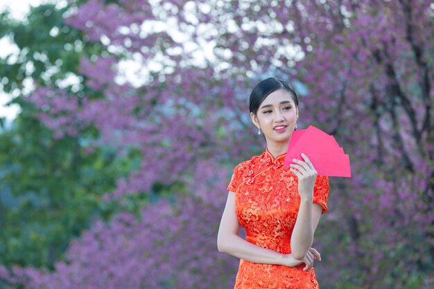 Schöne asiatische Frau zeigt etwas und nimmt rote Umschläge im chinesischen Neujahr