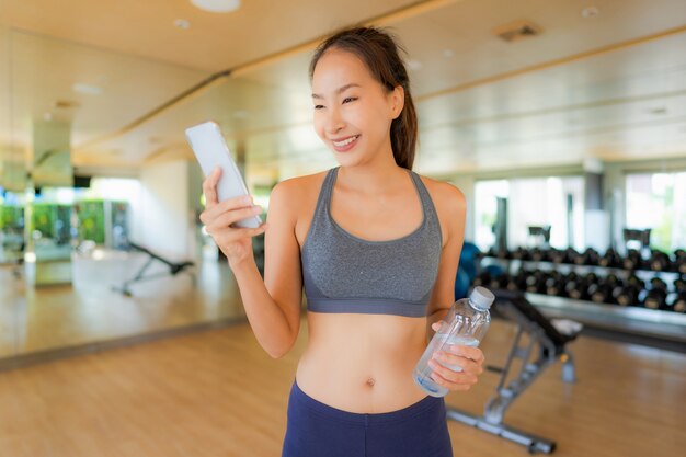 Schöne asiatische junge Frau des Porträts, die Handy in der Turnhalle verwendet