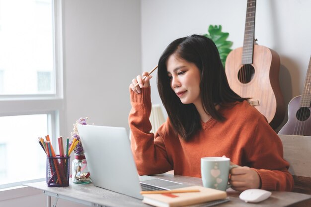 Schöne asiatische junge Frau kreative Freiberuflerin, die an einem Laptop-Computer arbeitet, der von zu Hause aus arbeitet