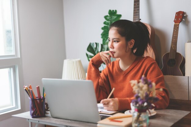 Schöne asiatische junge Frau kreative Freiberuflerin, die an einem Laptop-Computer arbeitet, der von zu Hause aus arbeitet