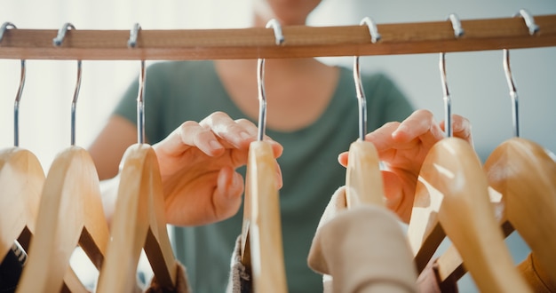 Schöne attraktive junge Asia-Dame, die ihre Mode-Outfit-Kleidung im Schrankwohnzimmer im Haus oder im Laden auswählt. Mädchen denken, was man Freizeithemd anziehen soll