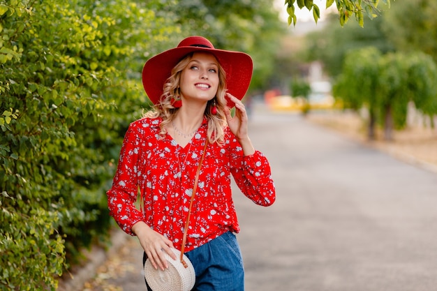 Schöne attraktive stilvolle blonde lächelnde Frau in strohrotem Hut und Bluse Sommermode-Outfit