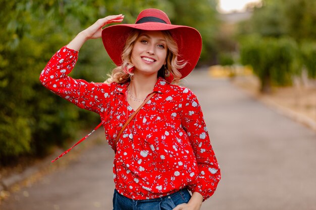 Schöne attraktive stilvolle blonde lächelnde Frau in strohrotem Hut und Bluse Sommermode-Outfit