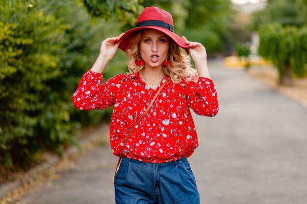 Schöne attraktive stilvolle blonde lächelnde Frau in strohrotem Hut und Bluse Sommermode-Outfit