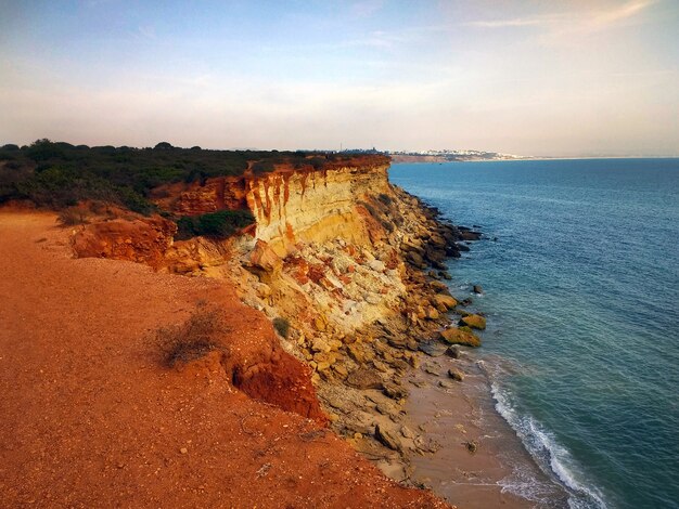 Schöne Aufnahme der Klippe bedeckt in Büschen neben einem Strand voller Felsen in Cádiz, Spanien.