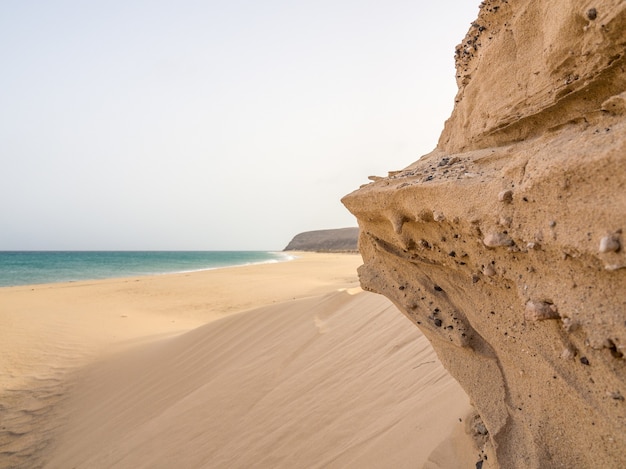 Schöne Aufnahme einer felsigen Küste mit weichem Sand und blauem Meer in Fuerte Ventura, Kanarische Inseln