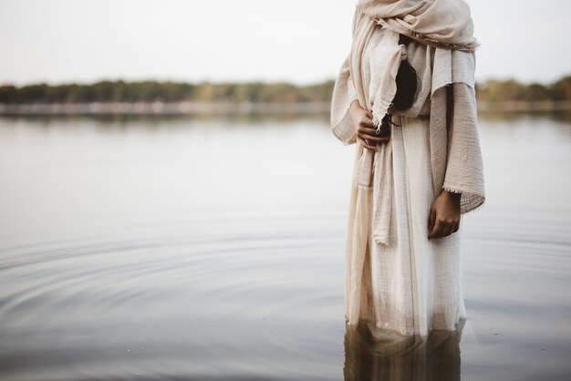 Schöne Aufnahme einer Frau, die ein biblisches Gewand trägt, während sie im Wasser steht