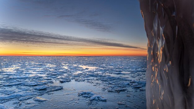 Schöne Aufnahme einer Winterlandschaft, einer Küstenlinie mit gebrochenem Eis, Schnee und Meerwasser bei Sonnenuntergang.