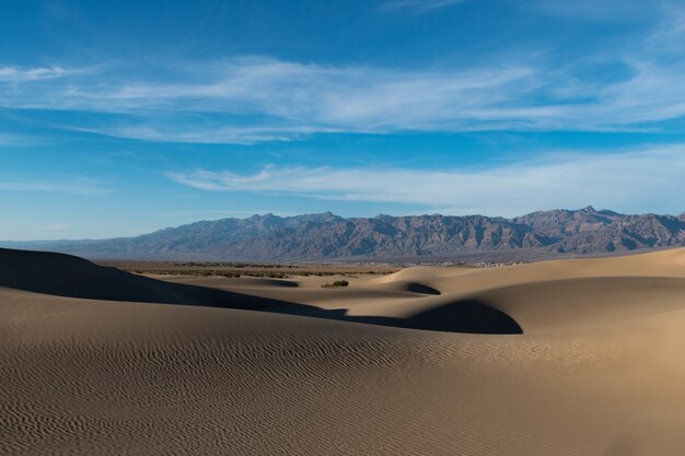 Schöne Aufnahme einer Wüste mit Spuren auf dem Sand und felsigen Hügeln unter dem ruhigen Himmel