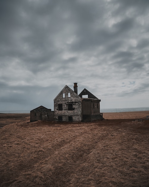 Schöne Aufnahme eines alten verlassenen und halb zerstörten Hauses in einer großen Brachfläche unter grauem Himmel