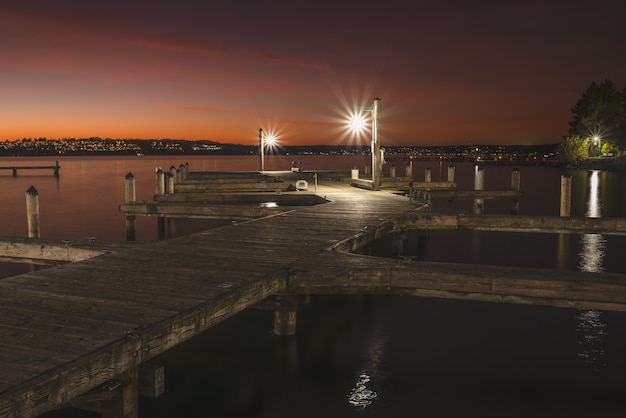Schöne Aufnahme eines beleuchteten hölzernen Piers im See um die Stadt bei Nacht