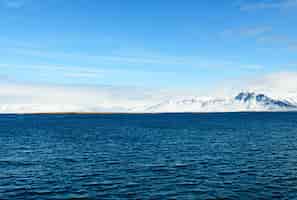 Kostenloses Foto schöne aufnahme eines blauen meeres voller wellen vor einem schneebedeckten berg in island