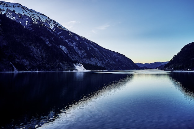 Schöne Aufnahme eines Flusses mit dem Spiegelbild der schneebedeckten Hügel und des Himmels