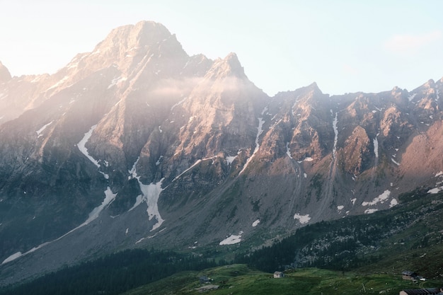 Kostenloses Foto schöne aufnahme eines hauses auf einem grasbewachsenen hügel mit bergen und einem klaren himmel