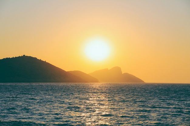 Schöne Aufnahme eines Meeres, das das Sonnenlicht mit einem Berg in der Ferne bei Sonnenuntergang reflektiert