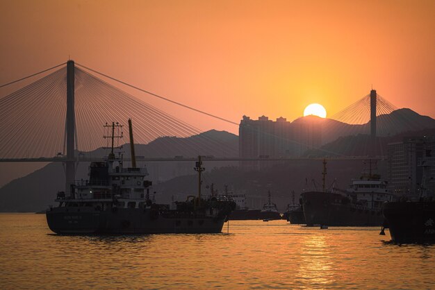 Schöne Aufnahme von Booten, die bei Sonnenuntergang im Meer mit einer Brücke im Hintergrund segeln