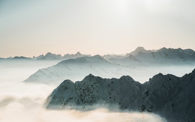 Schöne Aufnahme von schneebedeckten Berggipfeln über den Wolken mit einem klaren Himmel