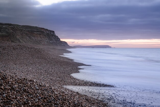 Schöne Aussicht auf das Meer, das bei Sonnenuntergang auf den mit Felsen und Kieselsteinen bedeckten Strand in Großbritannien trifft