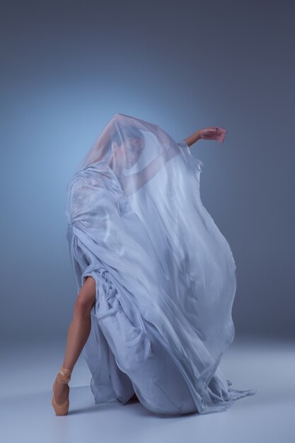 schöne Ballerina, die im langen blauen Kleid auf blauem Hintergrund tanzt