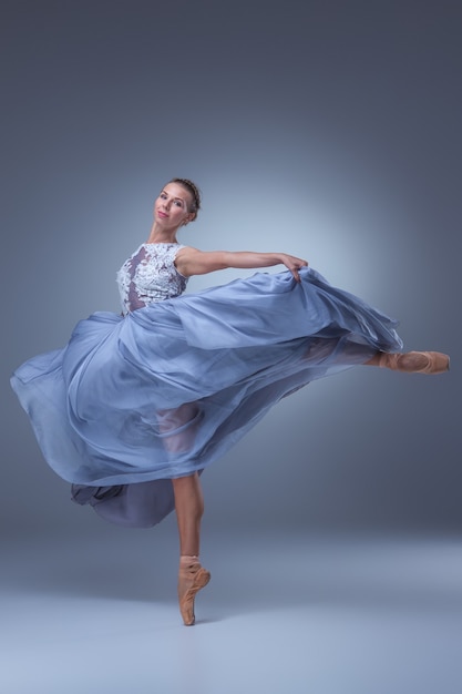 schöne Ballerina, die im langen blauen Kleid auf blauem Hintergrund tanzt